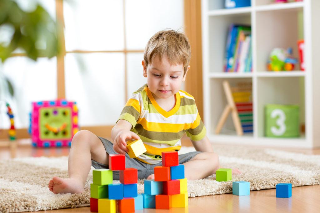 Kleines Kind in seinem Zimmer, das mit bunten Würfeln spielt und von pädagogischen Inhalten umgeben ist