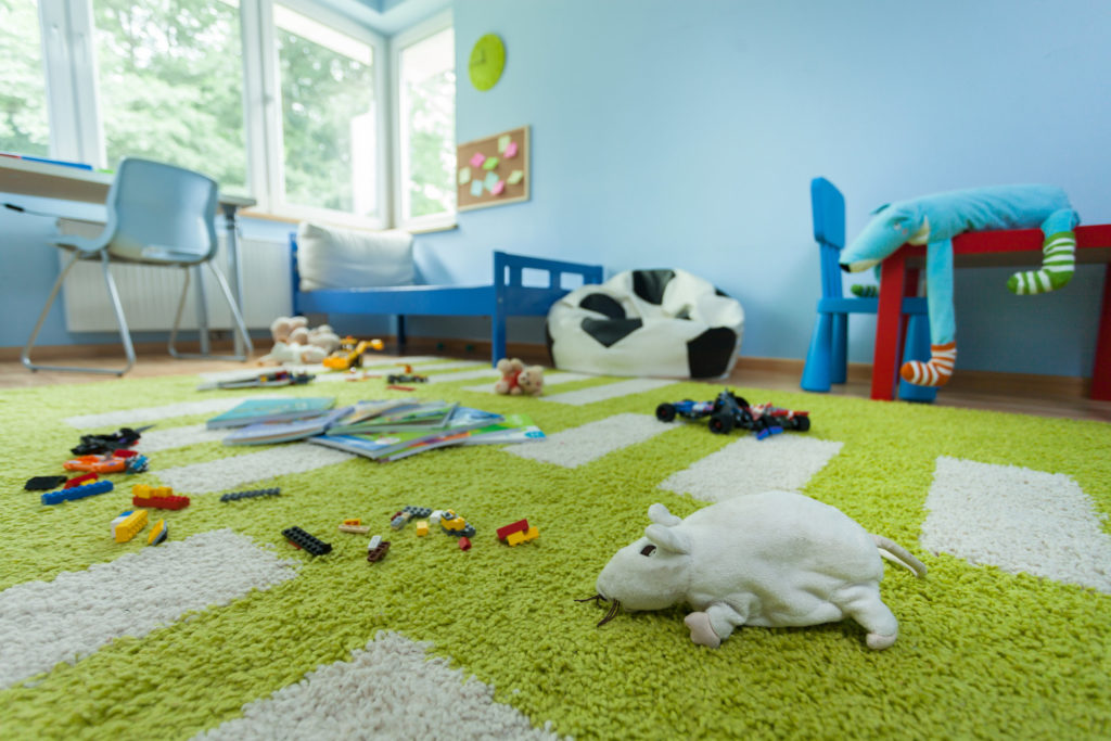 Kinderzimmer mit einem grünen Teppich, der wie Gras aussieht und auf dem Stofftiere und Spielzeug liegen