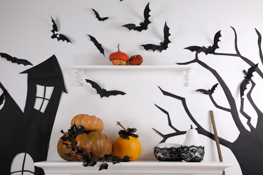 Hübsche Dekoration an einer weißen Wand aus schwarzen Papierfledermäusen, Kürbissen, einem schwarzen Papierbaum und einem ebenfalls schwarzen Papierspukhaus