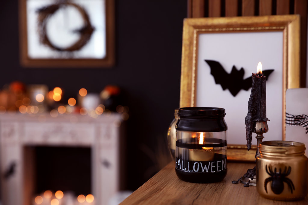 Op een dressoir in de woonkamer staat een glazen kandelaar met Halloween erop geschreven. Een fotolijstje met een vleermuis erop. Een zwarte kaars op een kandelaar brandt en de was druipt op het meubilair.