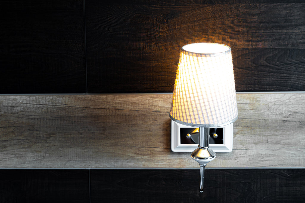 Nahaufnahme einer beleuchteten Nachttischlampe, die an einer Holzwand hängt.
