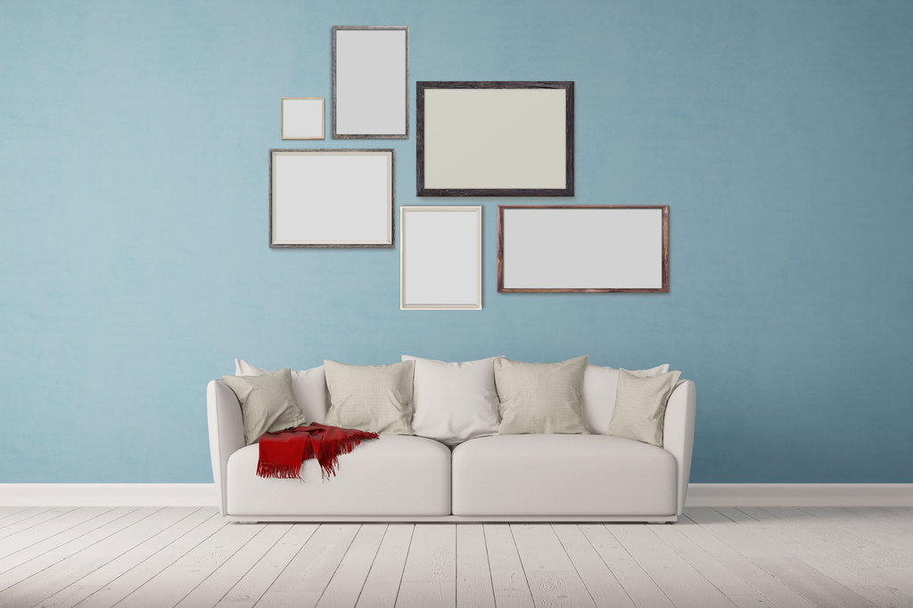 un bel divano beige siede su un parquet bianco di fronte a un muro blu. le cornici sono appese al muro in modo geometrico